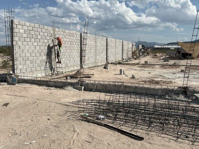 Muro de block de la bodega en obra, con castillos de varilla y un trabajador sobre una escalera.